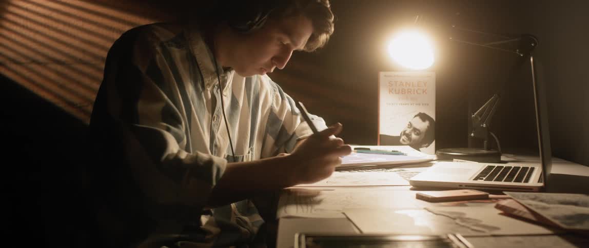 A boy wearing headphones sits at a desk and writes