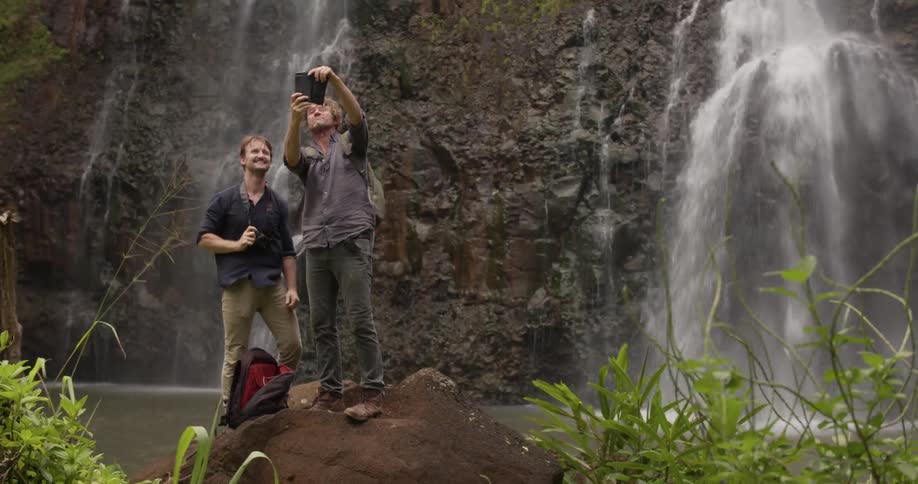 Two men pose for a photo at the bottom of the waterfall