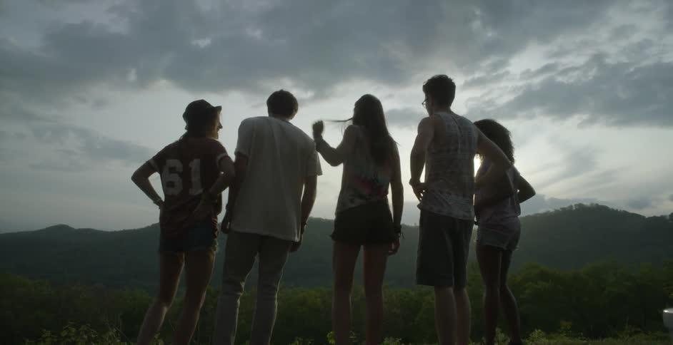 A group of young adults standing with their arms around each other while looking at the mountains