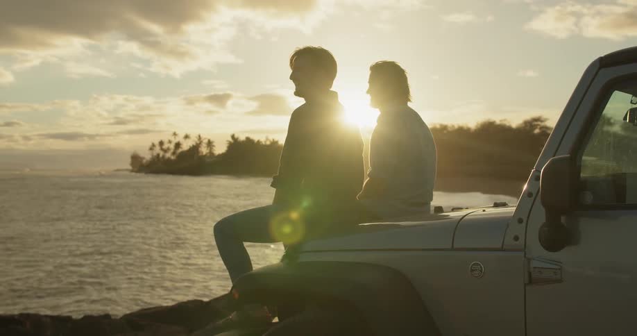 Two men sit on the hood of a truck by the water