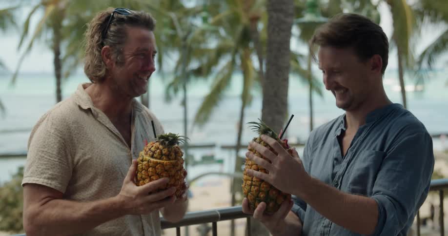 Men toast one another and sip from pineapples