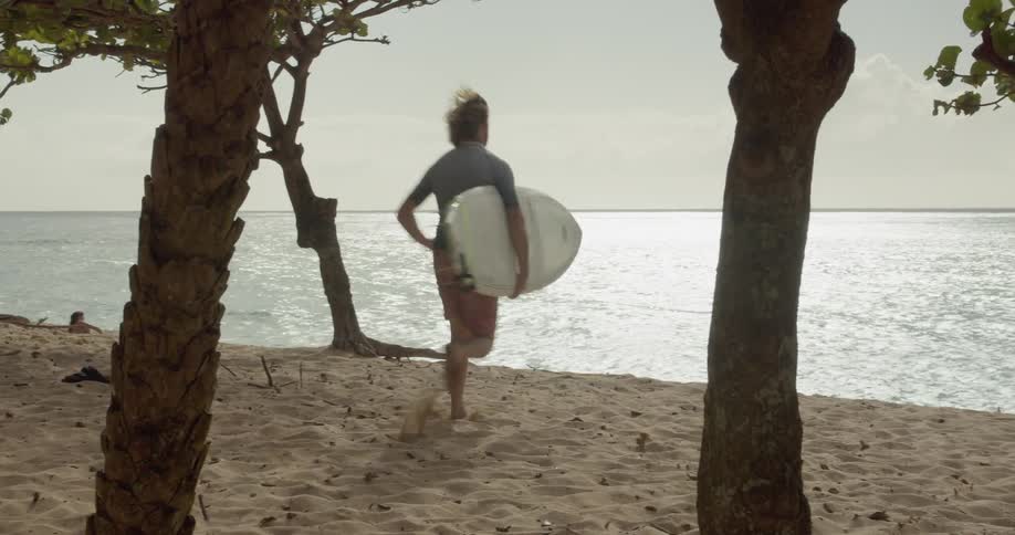 Man runs towards the ocean as he carries a surfboard
