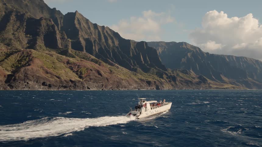 White boat travels in the water near a mountain