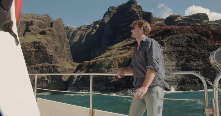 A man leans on the railing of a speeding boat