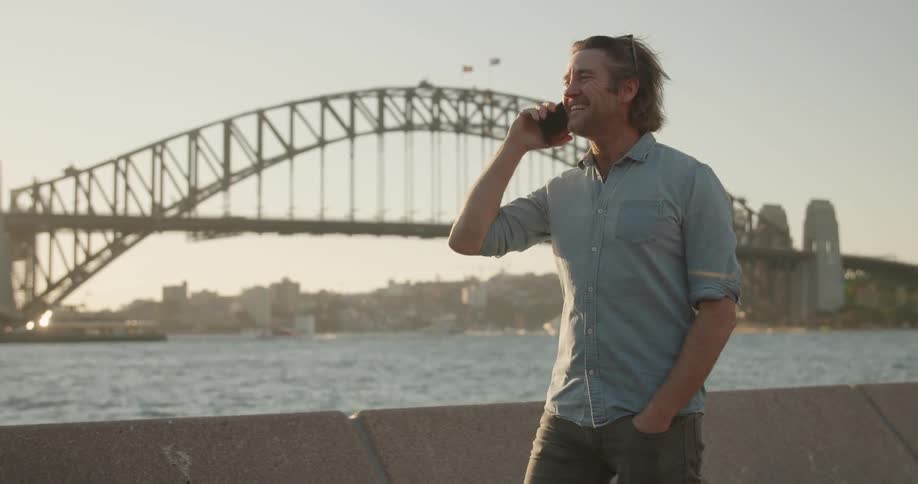 A man is talking on his cellphone in sydney harbor on a sunny day