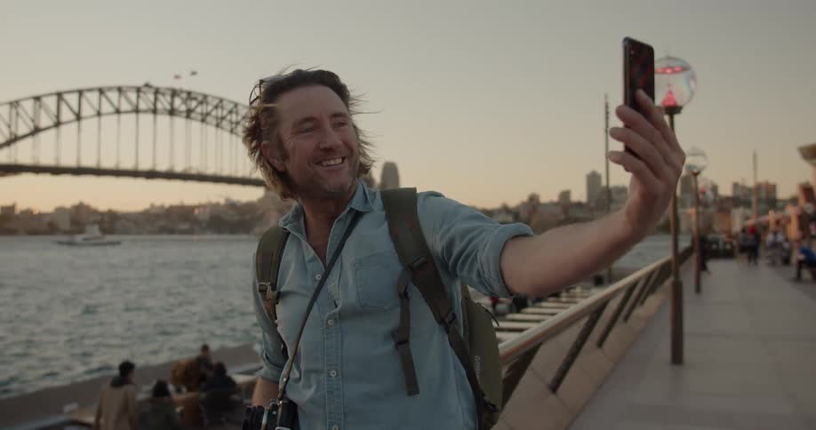 Man taking a selfie in front of the water near a bridge