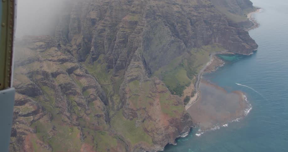 A plane flies above the mountains and blue water