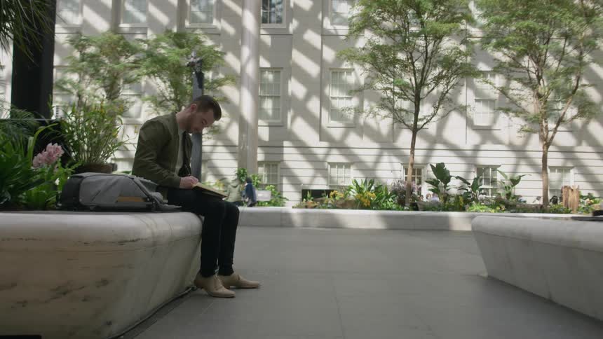 Man writes in a notebook while sitting outside in a courtyard