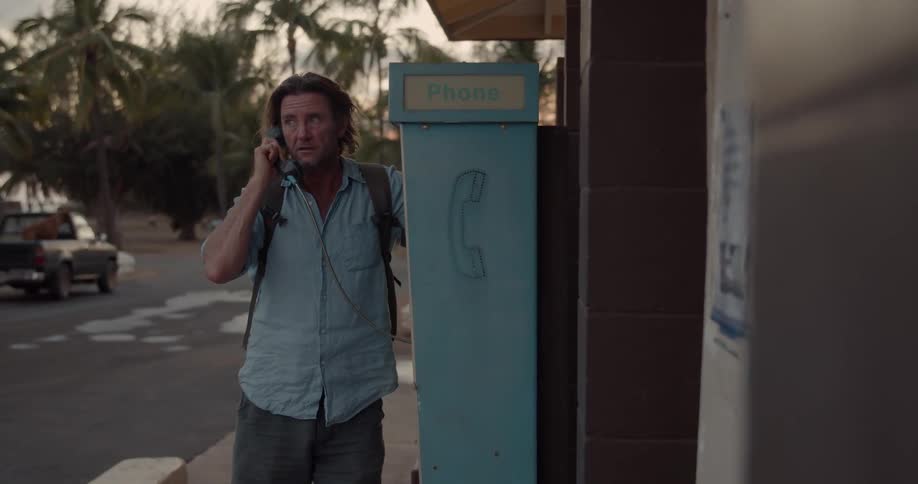 A man is talking on a public phone on the sidewalk