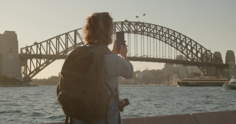 A man is taking pictures of a harbor in daylight with his cellphone
