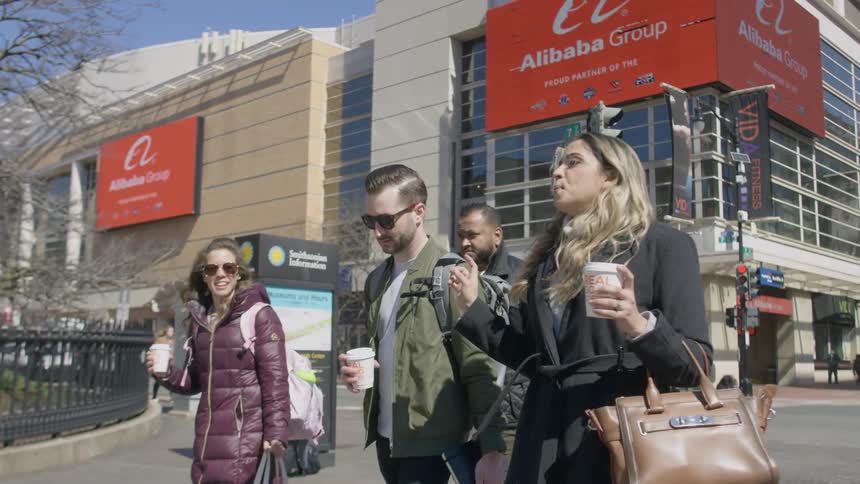 A woman is talking and holding a coffee cup as she walks with friends in a city in daylight