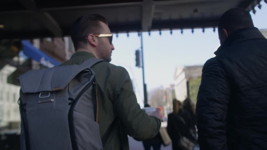 Two men are walking on a city sidewalk in daylight