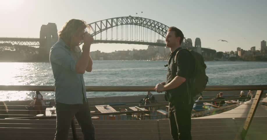 A man takes a photograph of another man by the water