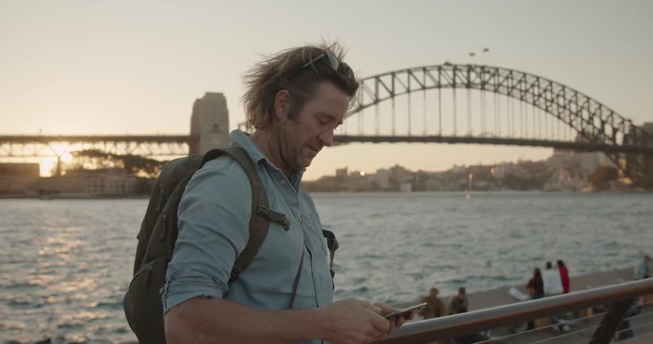Man uses cellphone to take a photo of birds flying near a bridge