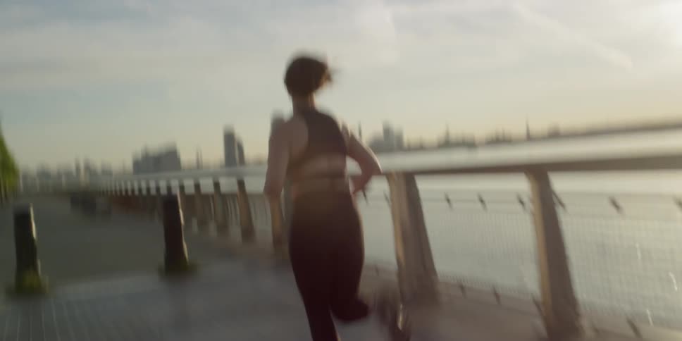 A woman jogs alongside a river at sunset