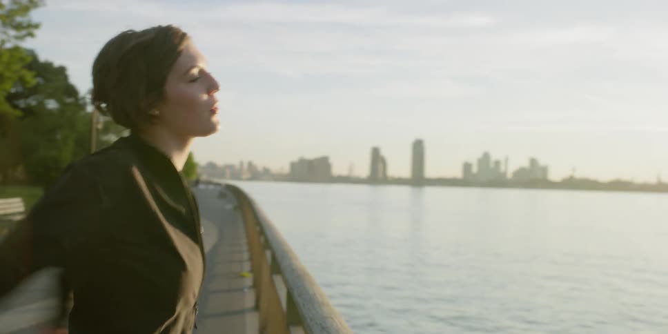 A woman is standing at a railing overlooking a harbor and stretching in daylight
