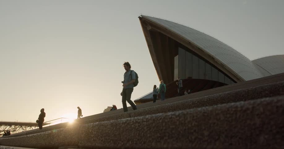 A man is descending the stairs outside the sydney opera house at sunset
