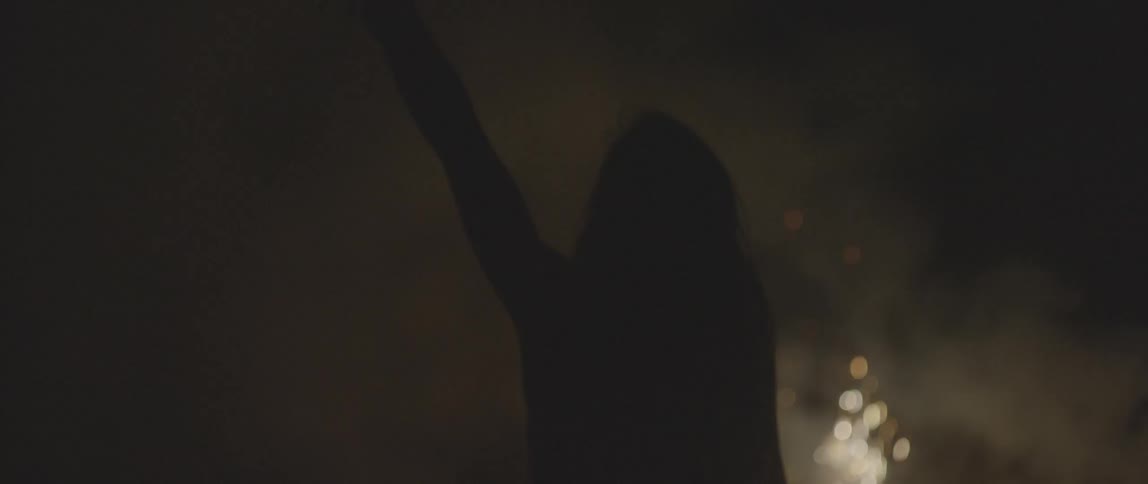 A woman is silhouetted by fireworks sparking in the distance