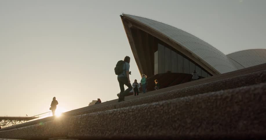 People walk up the stone steps towards the building at sunset