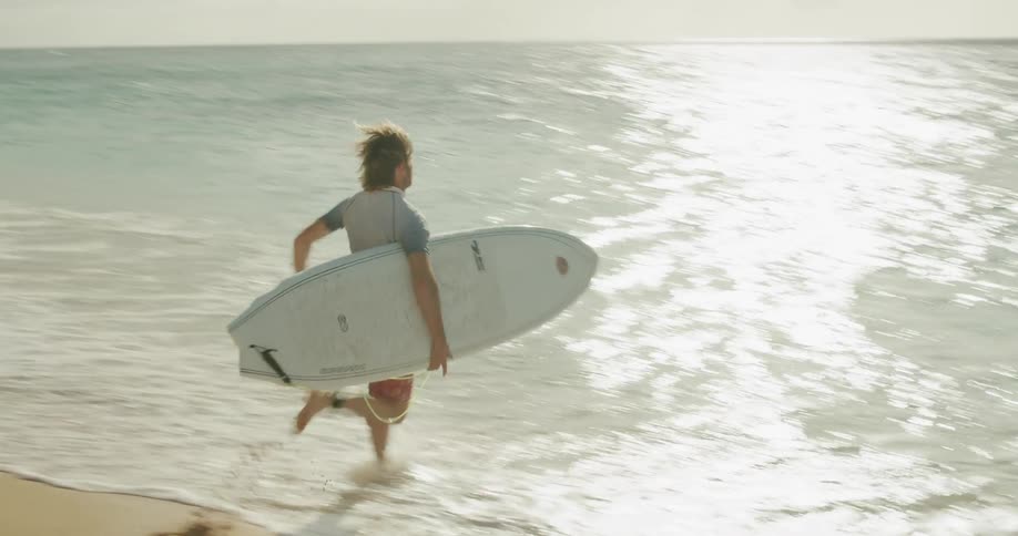 A man runs into the water with a surfboard