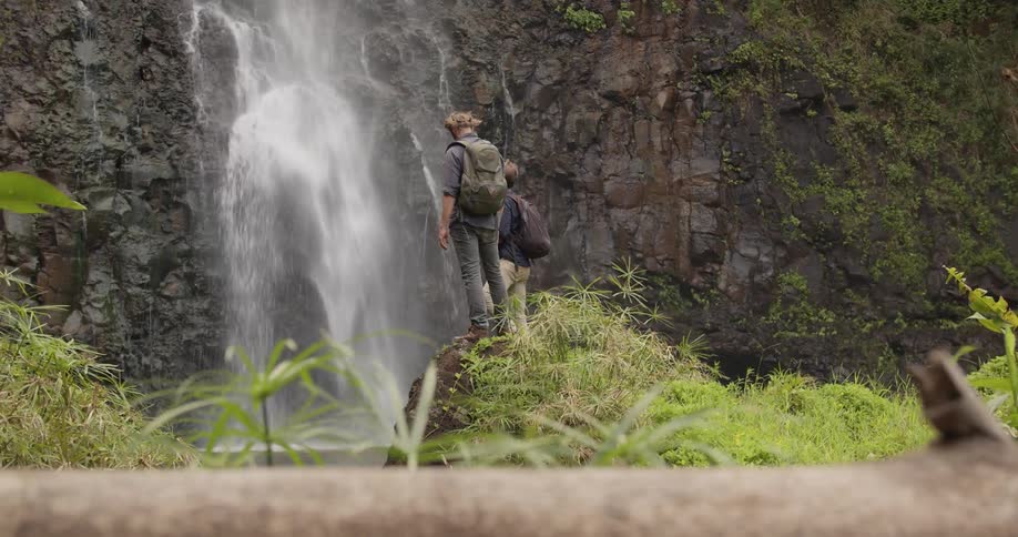 Two men stand on a rock and watch a waterfall