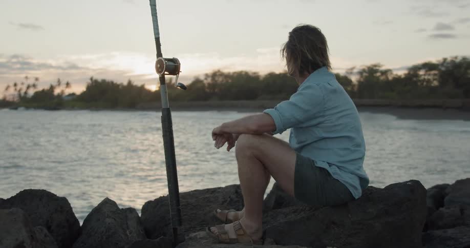 Man sitting on rocks, looking out over the water while fishing