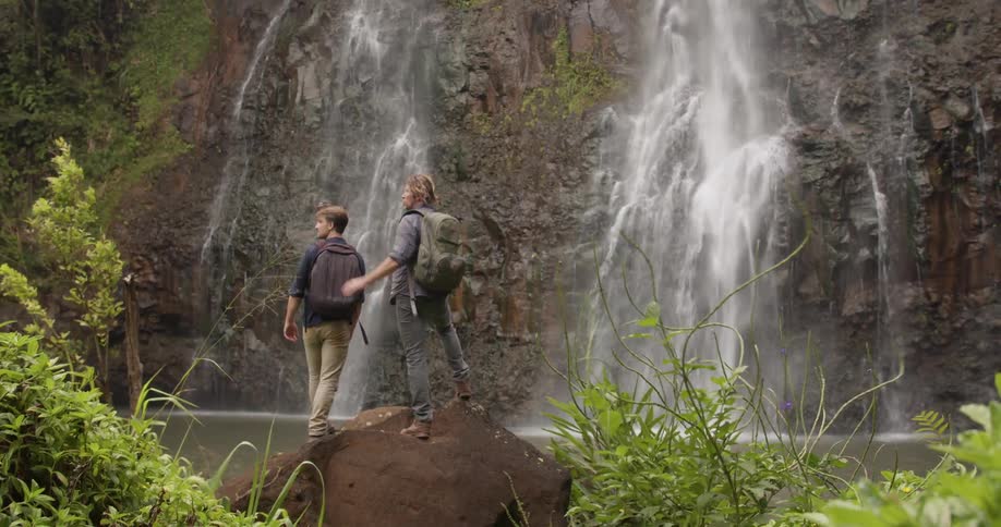 Two men stand at the bottom of a waterfall