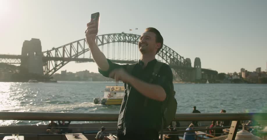 Man taking a selfie in front of the water near a bridge