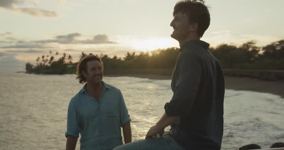 Two men laugh near the shore at sunset
