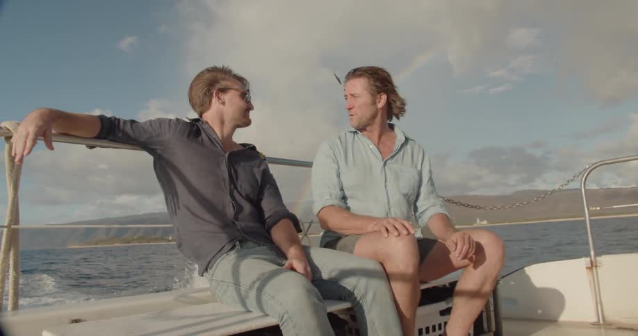 Two men ride on the back of a speeding boat