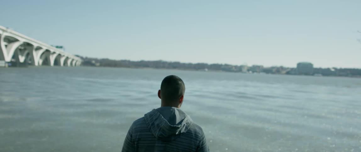 A man is looking across a river in an urban area on a sunny day