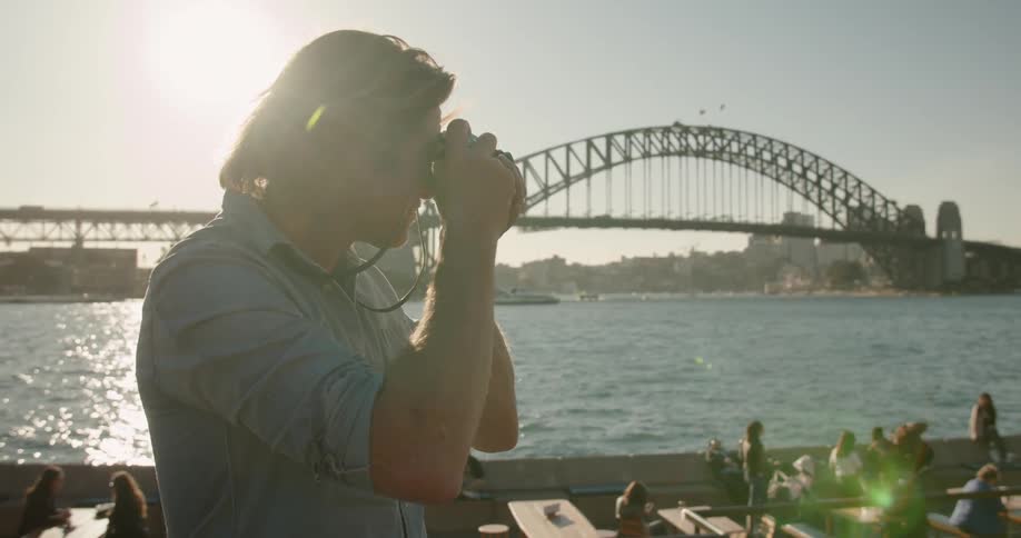A man takes a photograph by the water