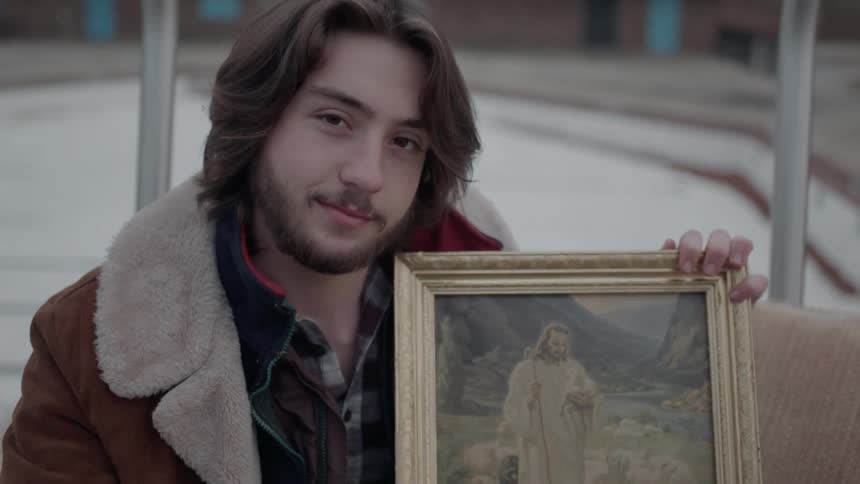 A man is smiling as he holds an image of jesus outside in daylight