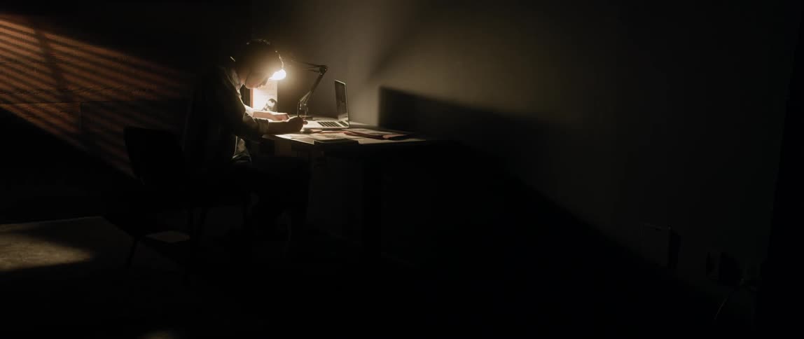A man sits at a desk in a dark room