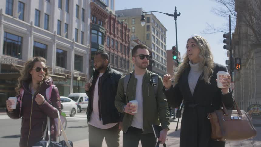 A group of friends talk while walking down a city sidewalk