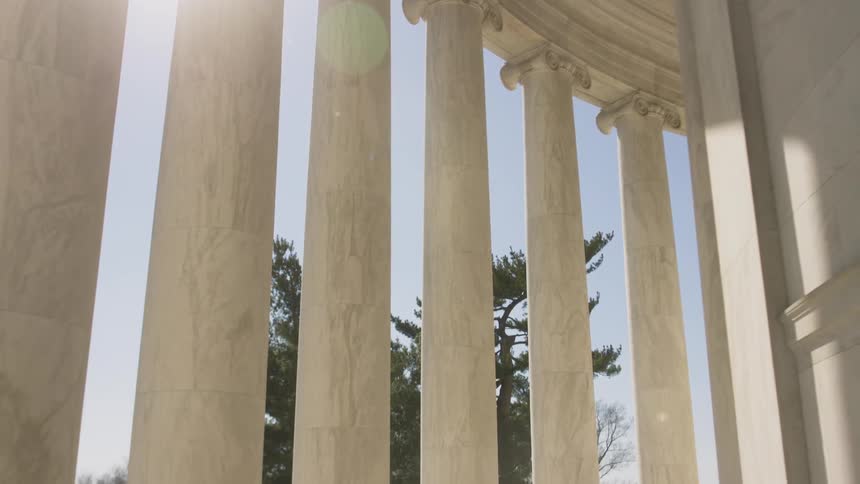 People walk past tall pillars on a sunny day