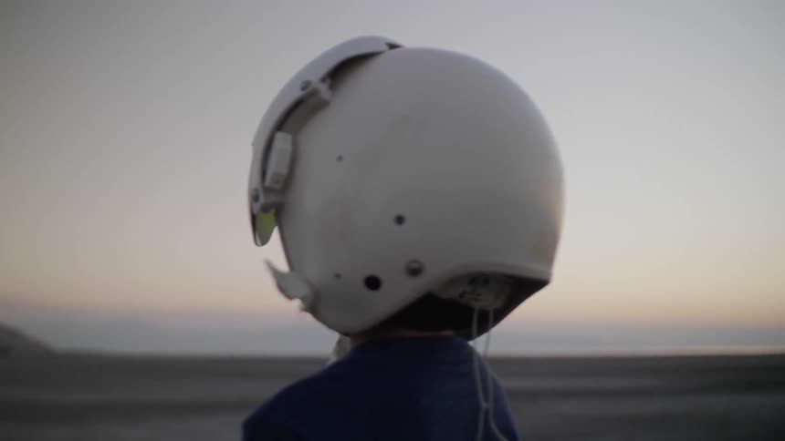 A boy in a pilot helmet stares across the desert at a mountain