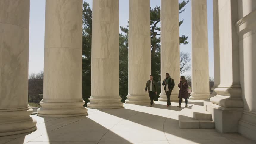Three people walk by the large columns