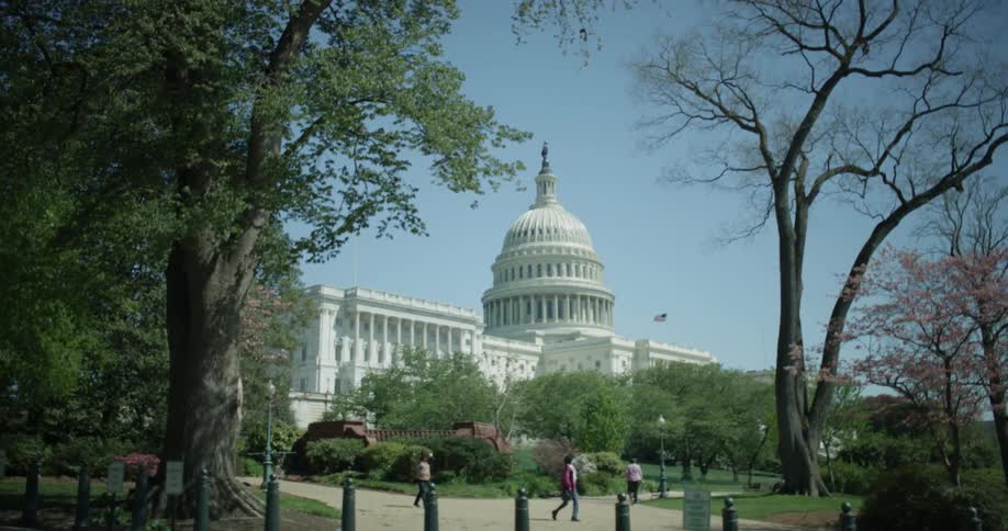 People are walking in a park outside a capitol building on a sunny day