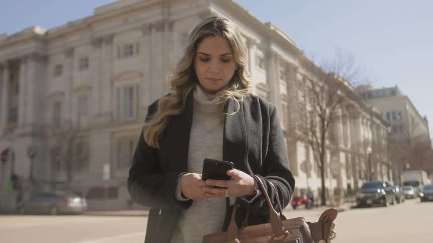 A woman uses her phone on the street by a large building