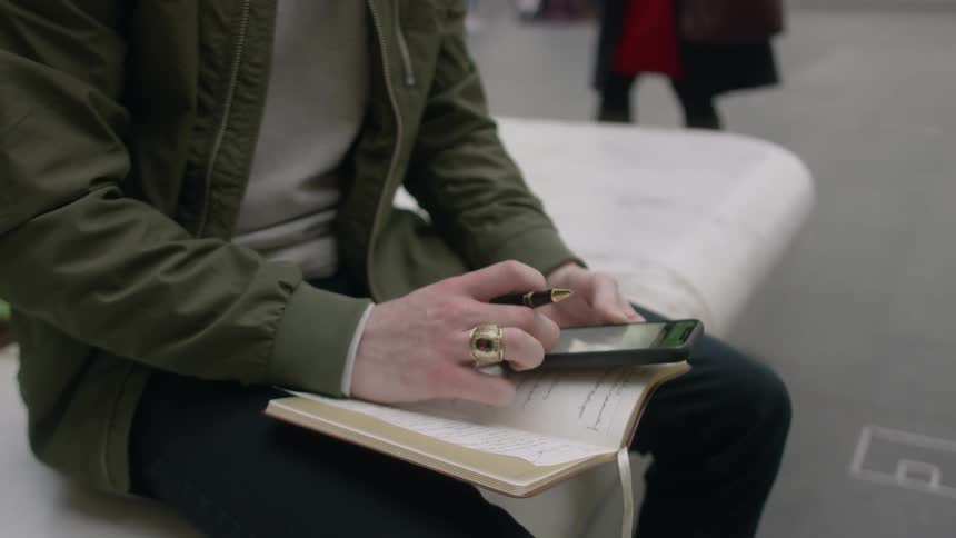 A man is writing and using their phone outside