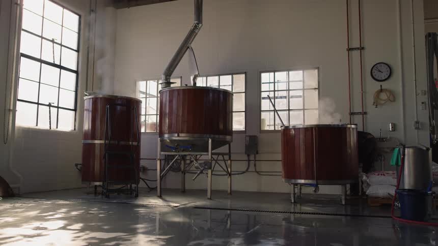 Steam rises from large vats in a brewery