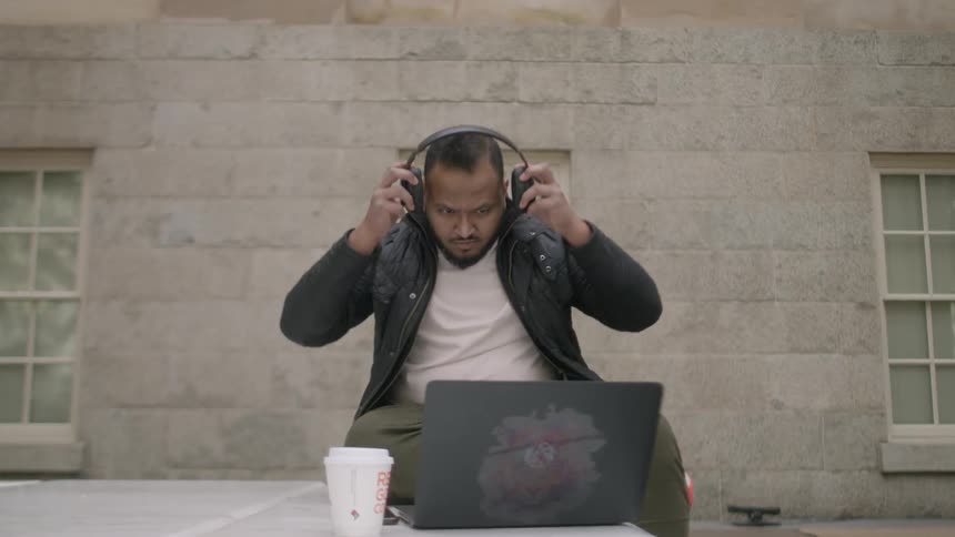 A man using a laptop outside puts on headphones