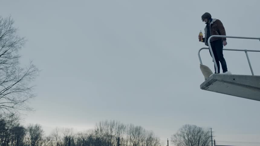 Man stands at the edge of a diving board and drinks from a bottle