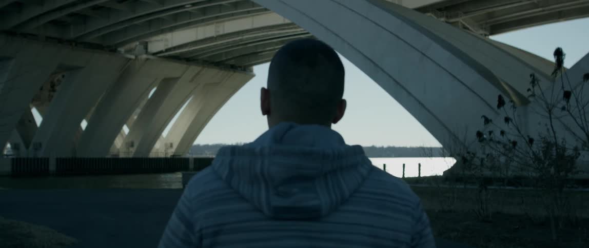 Man in hoodie walks under bridge