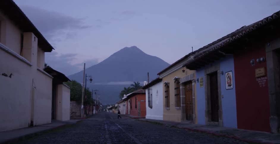 A person walks down a road between buildings near a mountain