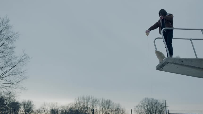 A man stands on an outdoor diving platform and empties a bottle