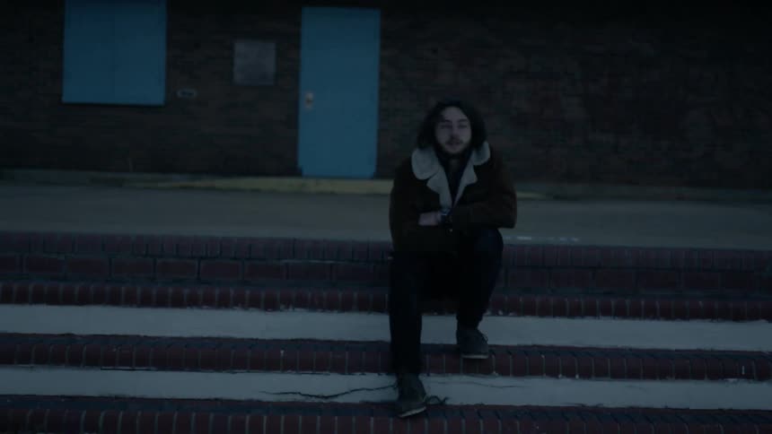 A man is sitting on stairs outside a building in winter at dusk