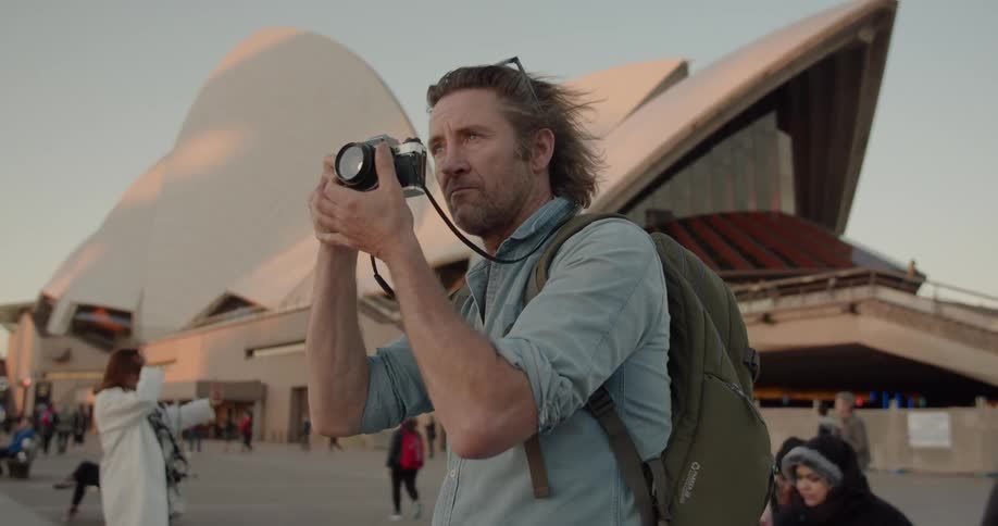 A man is taking pictures outside the sydney opera house during the day