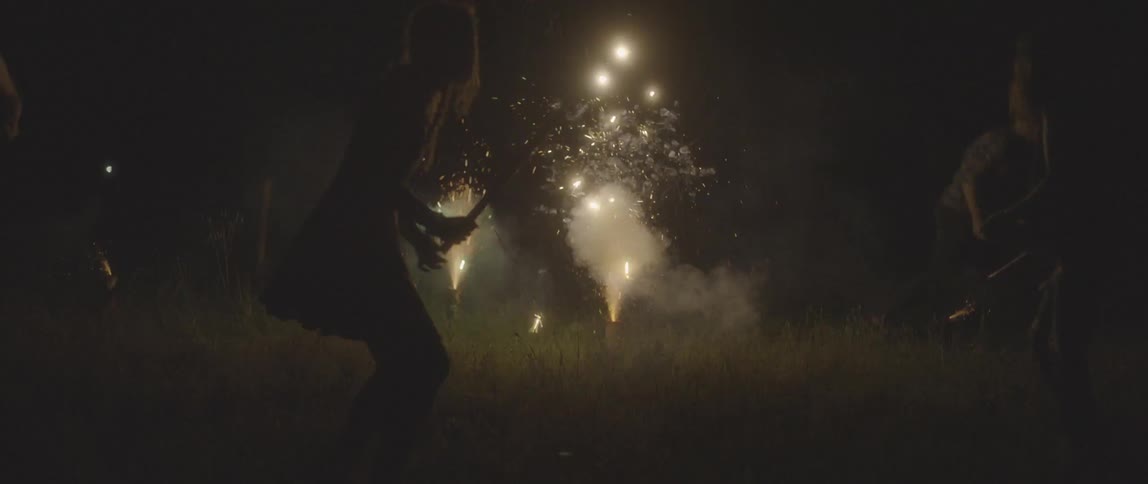 A girl running in a field as fireworks explode behind her
